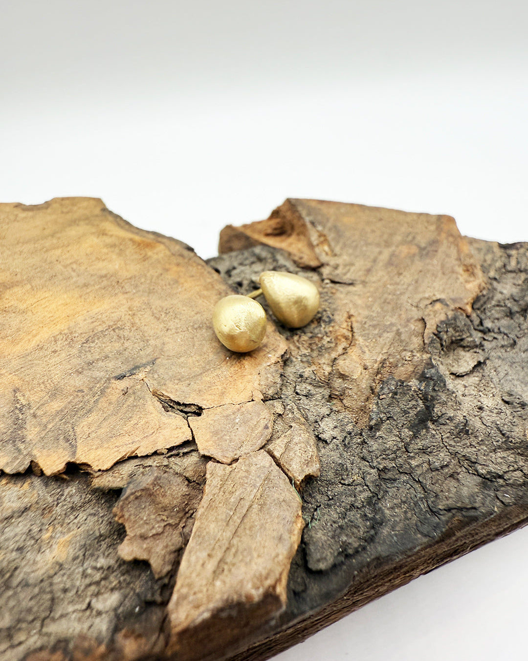 Gold earrings on a piece of textured wood