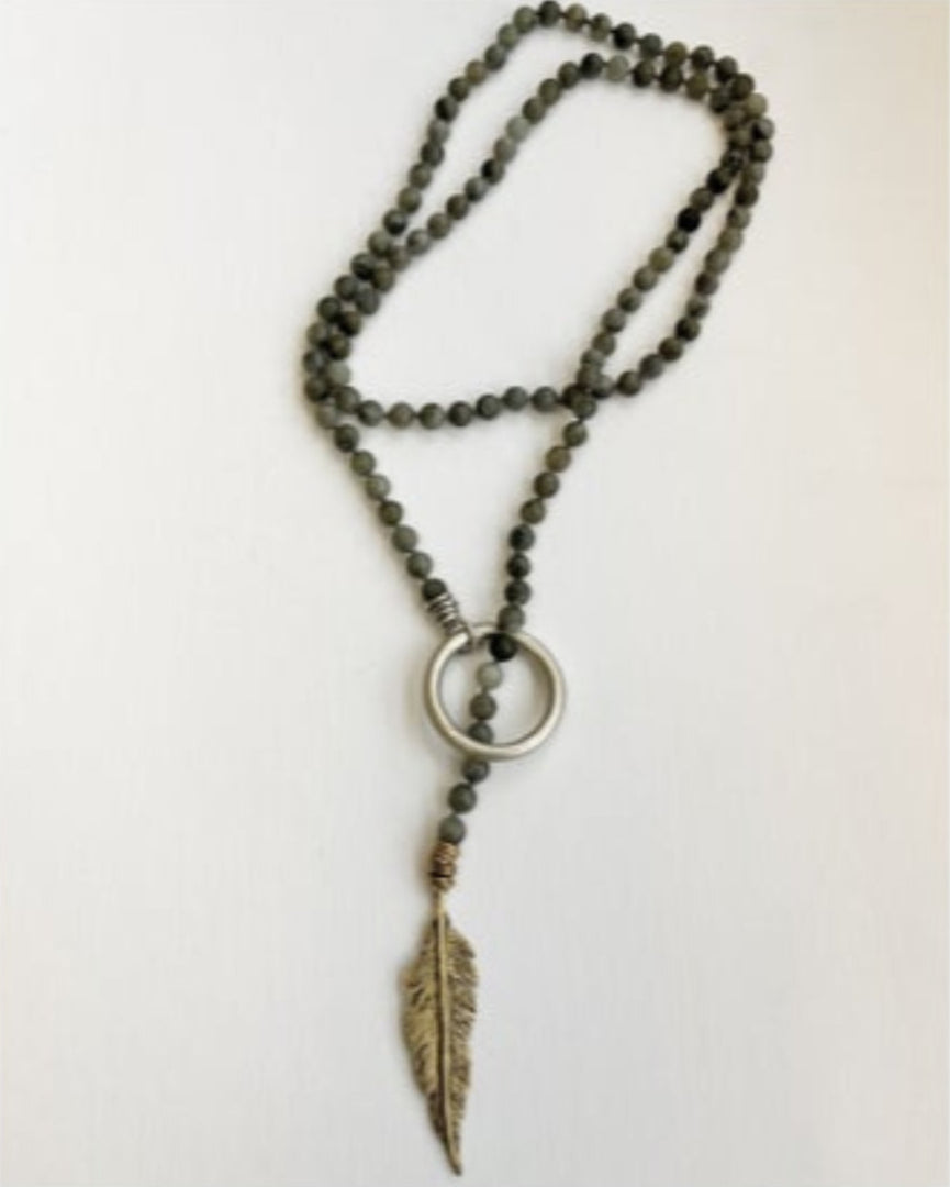 Necklace with beaded chain, gold circular accent and feather pendant on a white background