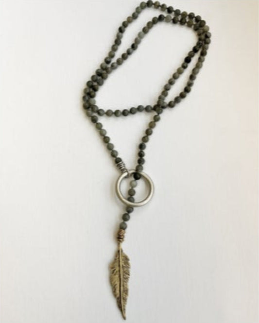 Necklace with beaded chain, gold circular accent and feather pendant on a white background