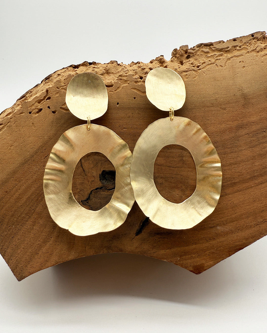 Gold hoop earrings on a wooden block with a white background