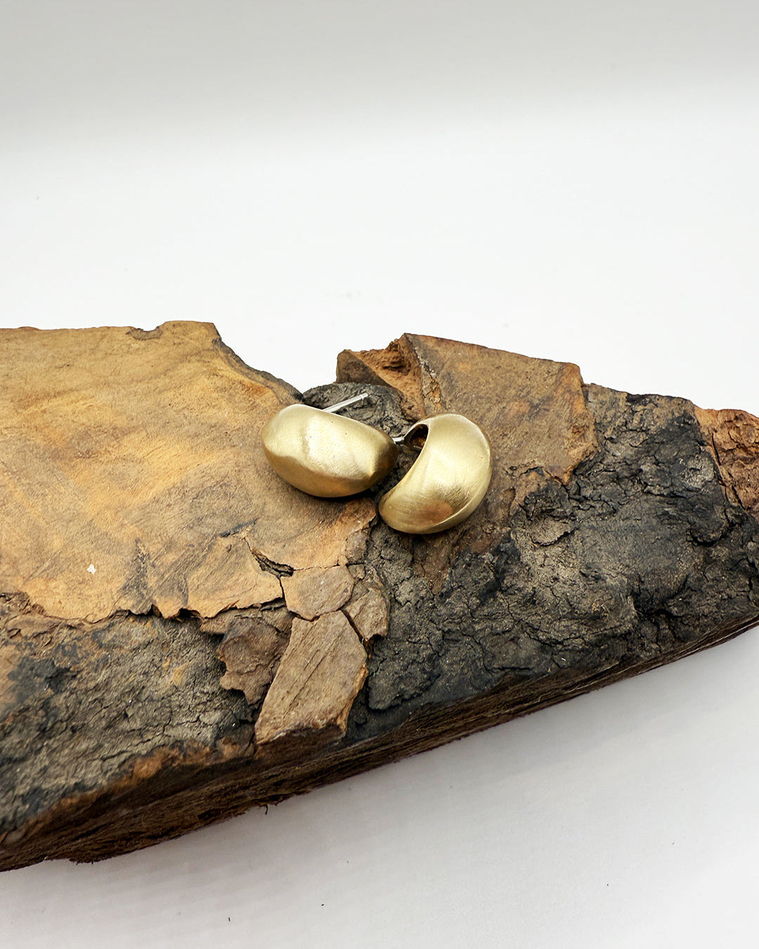 Gold earrings on a piece of wood with a white background