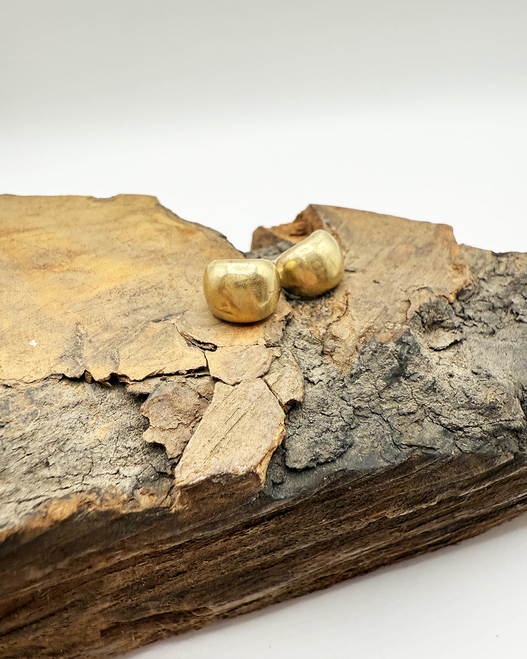 Gold earrings on a piece of wood with a white background