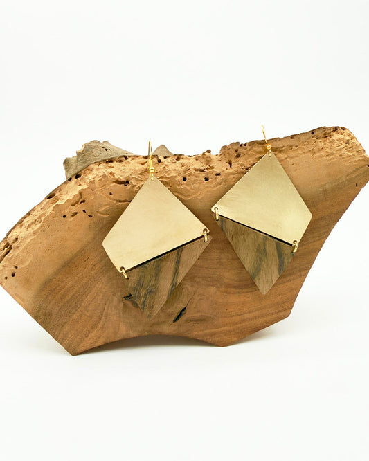 Gold geometric earrings on a wooden block with a white background