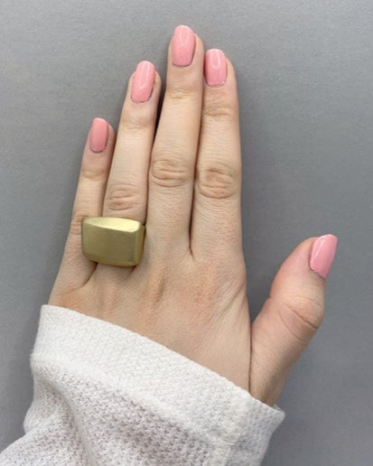 Hand wearing a statement bronze ring with pink nail polish against a gray background