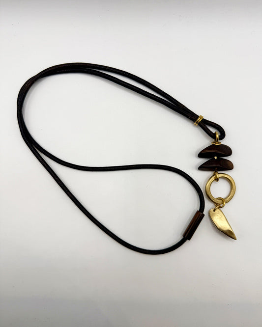 Necklace with black cord and gold pendant on a light gray background