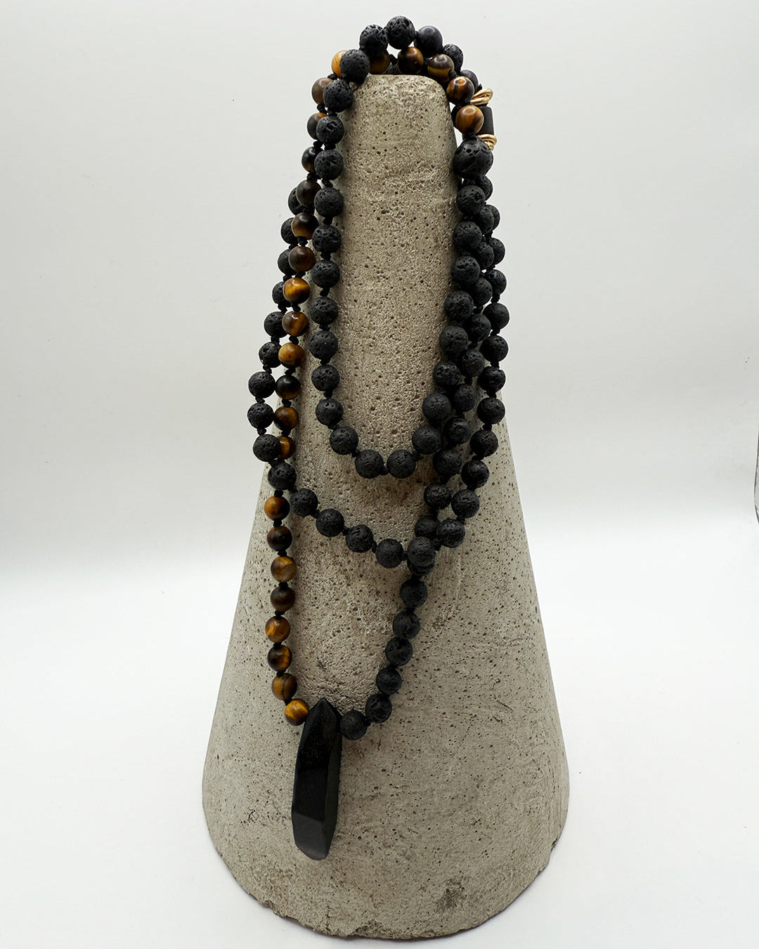 Black beaded necklace with a large pendant on a gray stand against a white background