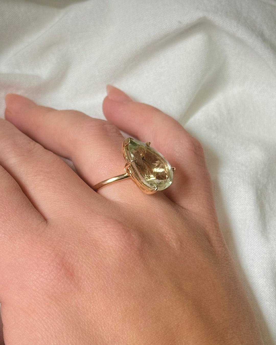 Hand wearing a gold ring with a large gemstone on a white fabric background
