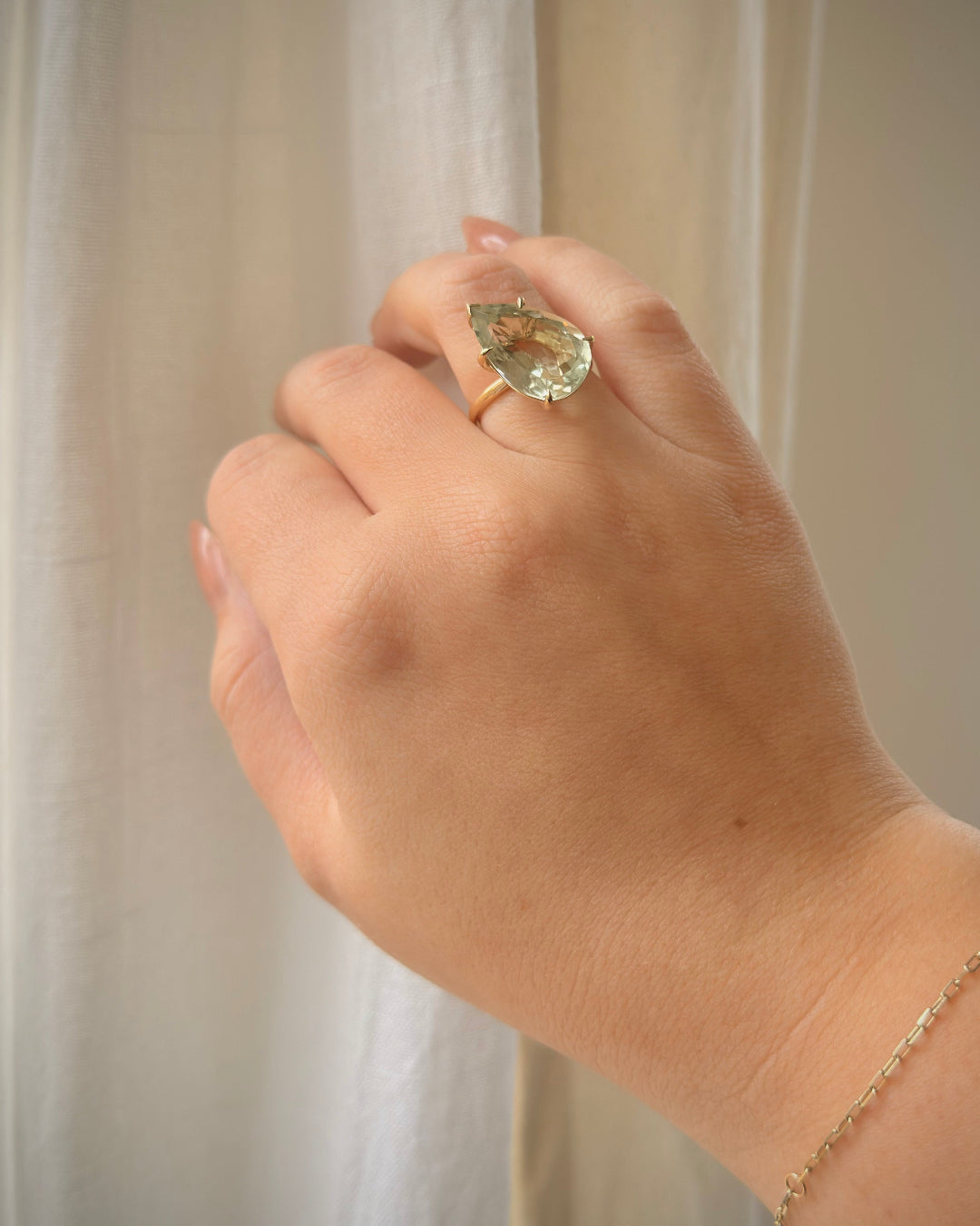 Hand wearing a ring with a green gemstone against a neutral background