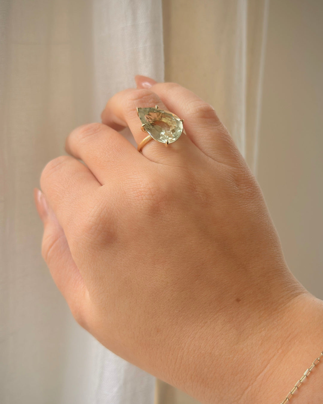 Hand wearing a ring with a green gemstone against a neutral background