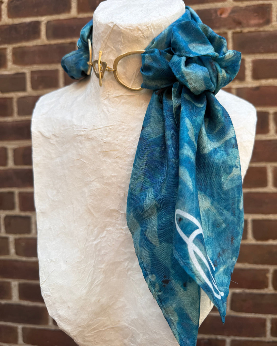 Mannequin head with a blue patterned scarf tied around its neck against a brick wall.