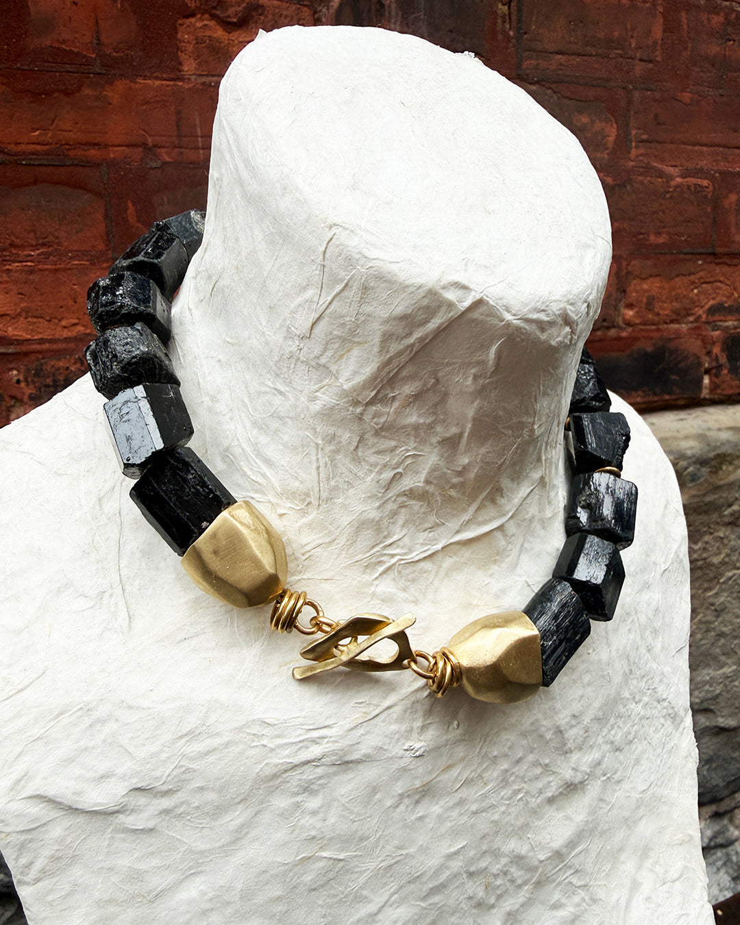 Necklace with black and gold beads on a mannequin head against a rustic wooden background