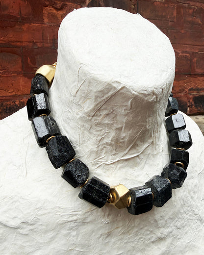 Necklace with black and gold beads on a mannequin head against a wooden background