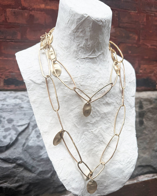 Gold chain necklace on a white mannequin bust against a rustic wooden background