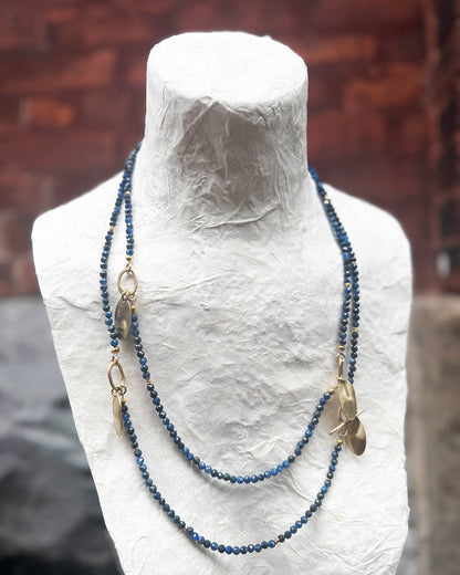 Blue beaded necklace on a mannequin bust against a brick wall background