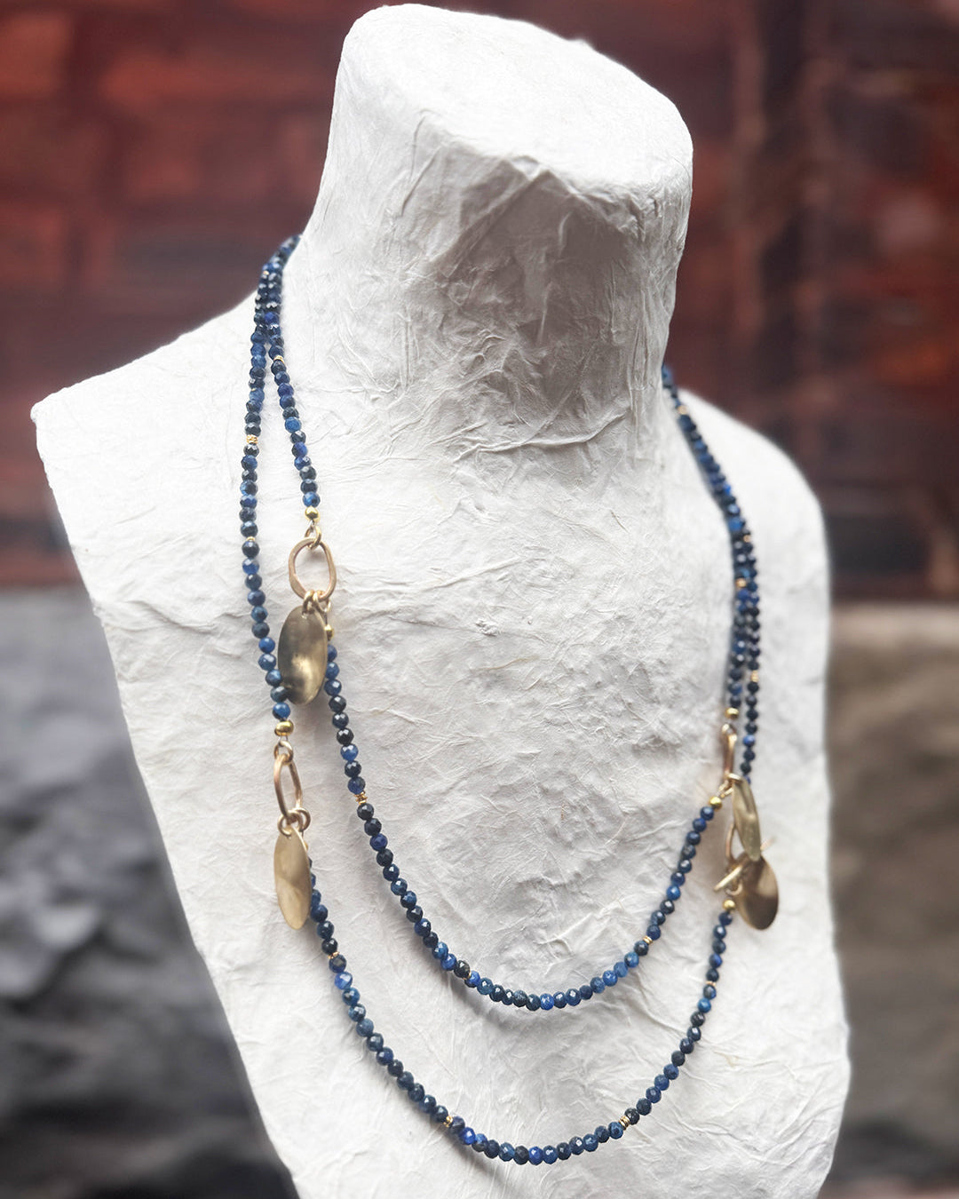 Necklace with blue beads and gold accents on a mannequin bust against a brick wall.