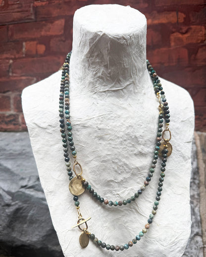 Necklace with beads and pendants on a mannequin bust against a brick wall.