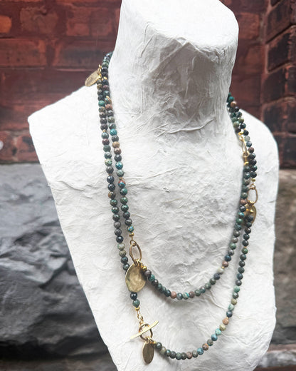 Necklace with beads and gold accents on a mannequin bust against a brick wall.