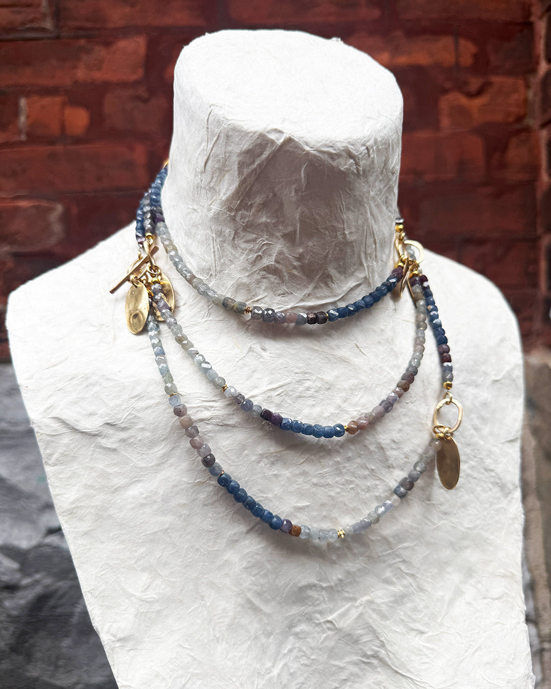 Necklace with blue beads and gold accents on a mannequin against a brick wall.