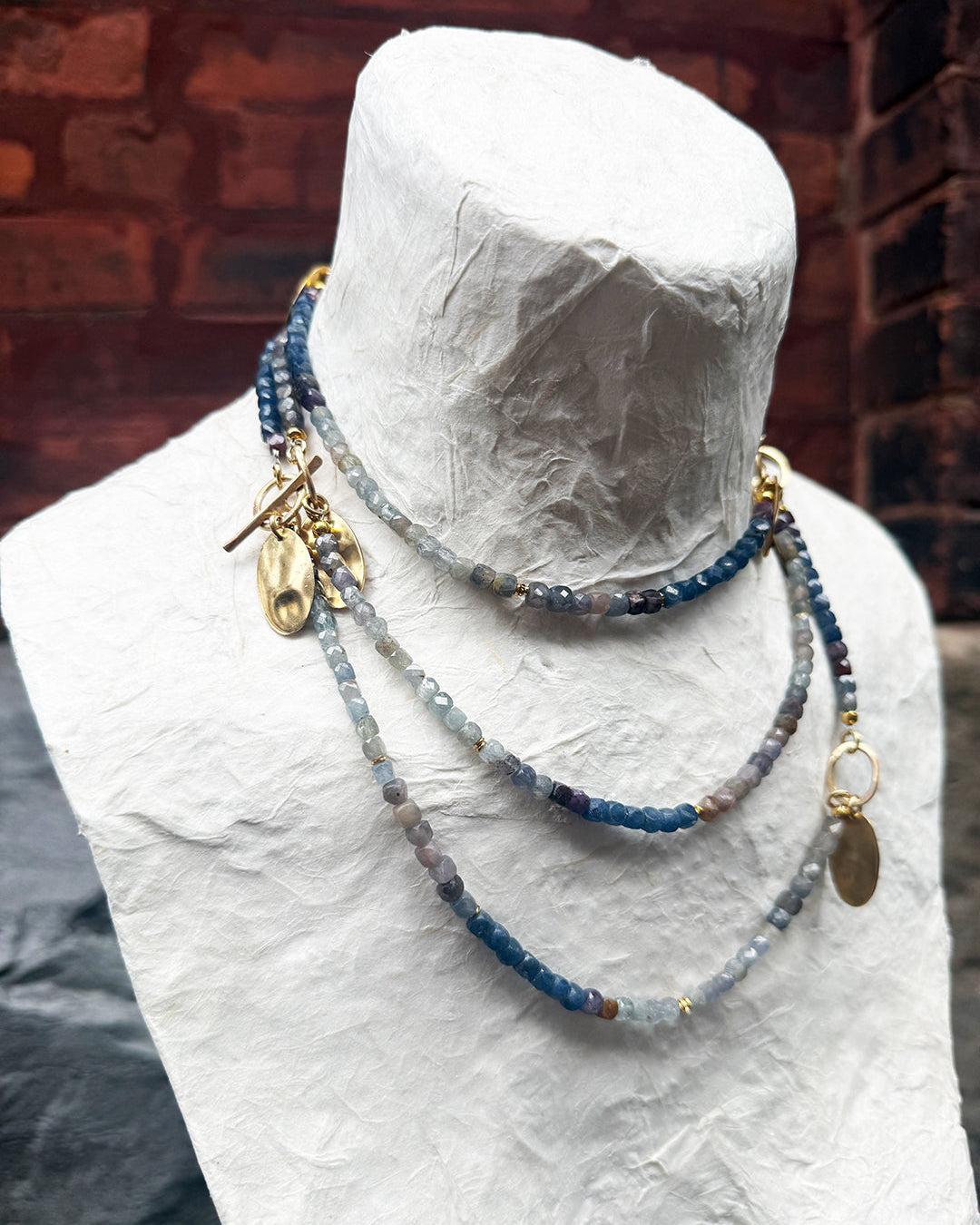 Necklace with blue beads and gold accents on a mannequin bust against a brick wall.