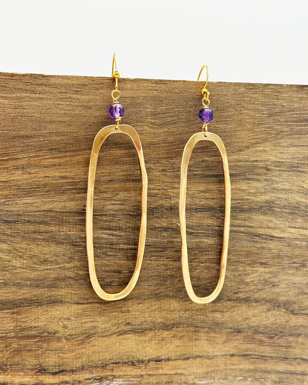 Gold hoop earrings with purple beads on a wooden surface