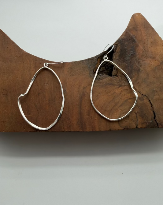 Silver hoop earrings on a wooden block with a white background