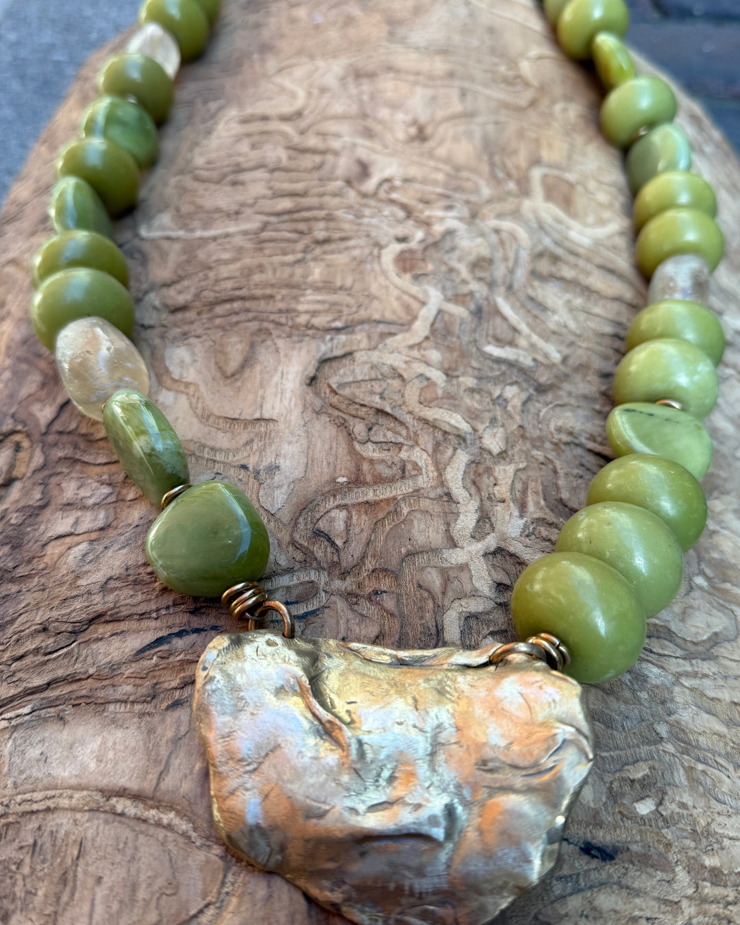 Necklace with green beads and a large bronze shell pendant on a wooden surface