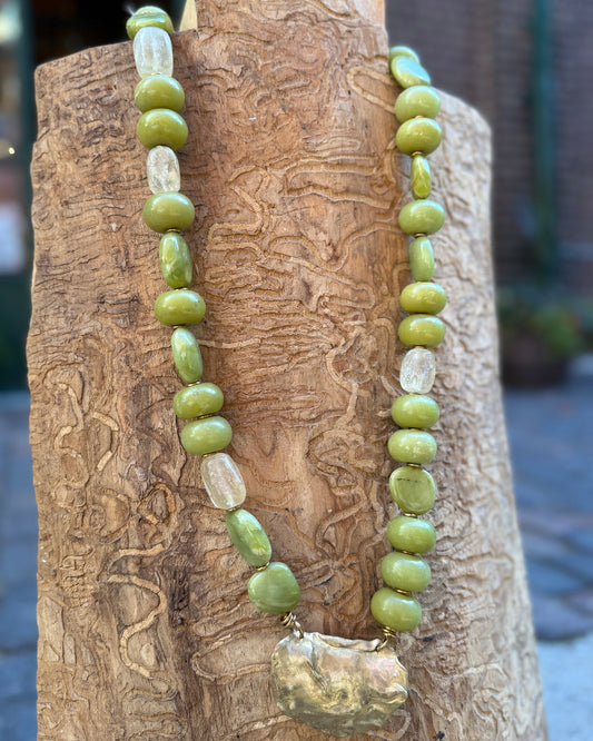 Necklace with green beads and a large bronze pendant on a wooden surface