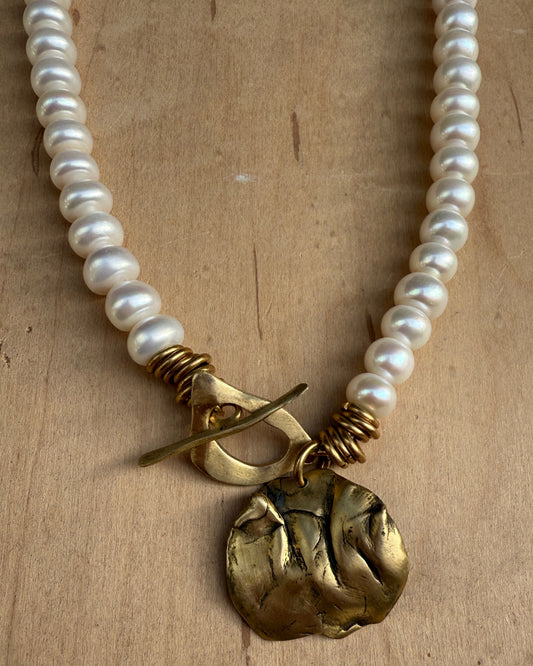 Pearl necklace with a gold pendant on a wooden surface