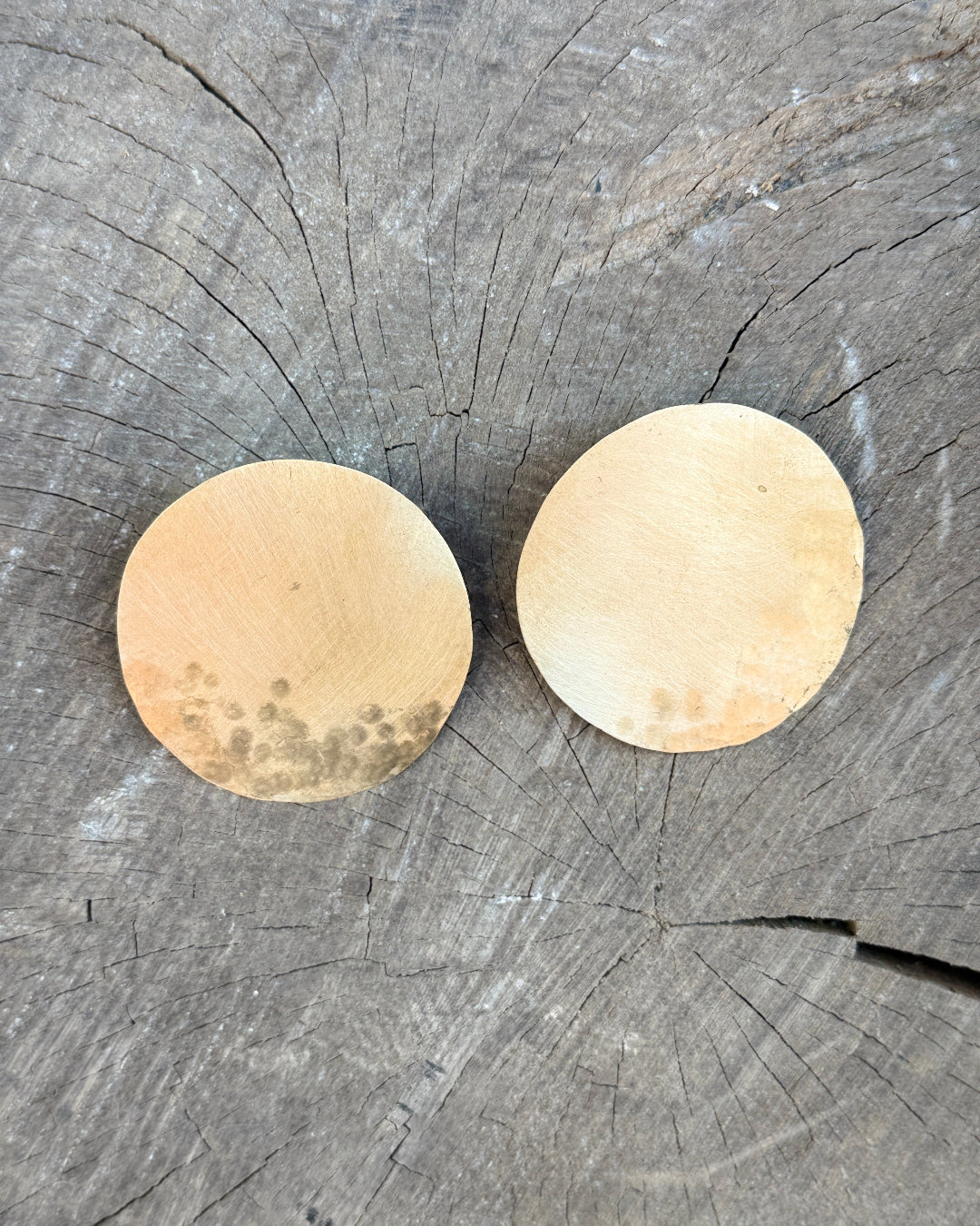 Two bronze circular earrings on a wooden surface