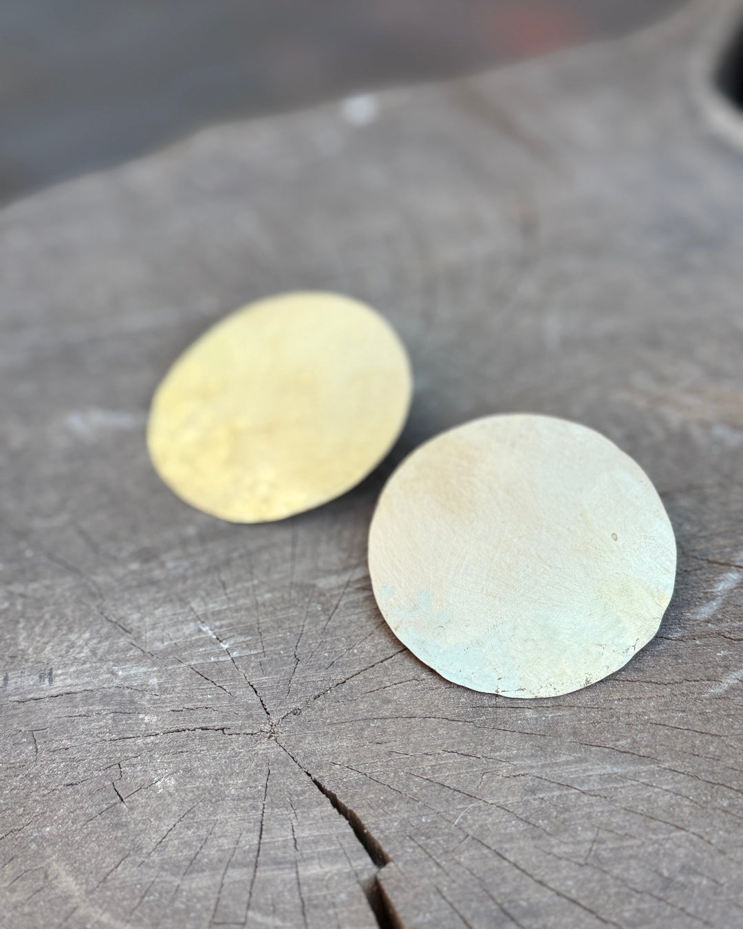 Two round metallic earrings on a wooden surface