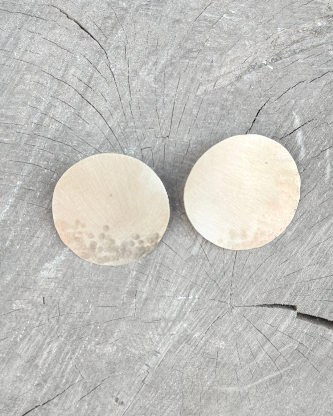 Two gold circular earrings on a wooden surface