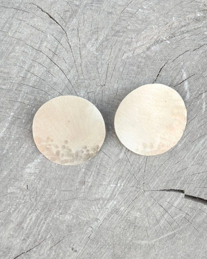 Two gold circular earrings on a wooden surface