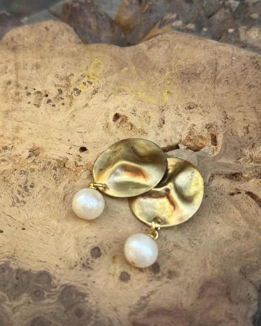 Textured bronze earrings with pearls on a stone surface