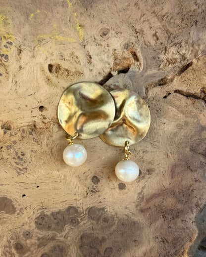 Gold earrings with pearl drops on a textured stone surface
