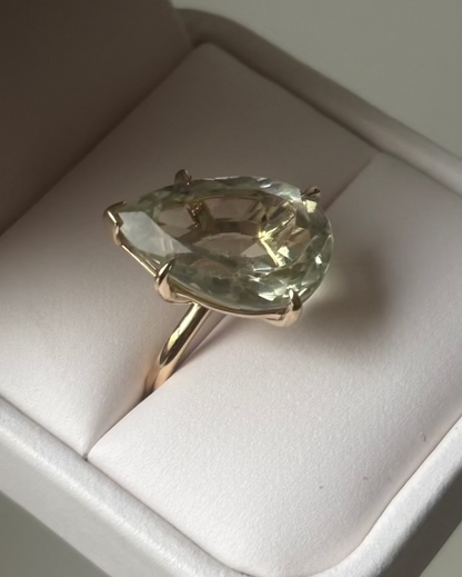 Gold ring with a large green pear-shaped gemstone in a cream ring box. 