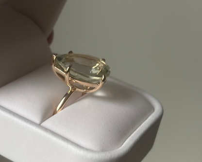 Gold ring with a green pear-shaped gemstone in a white ring box. 