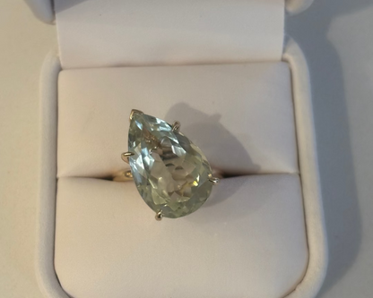 Gold ring with a pear shaped green gemstone in a white ring box. 