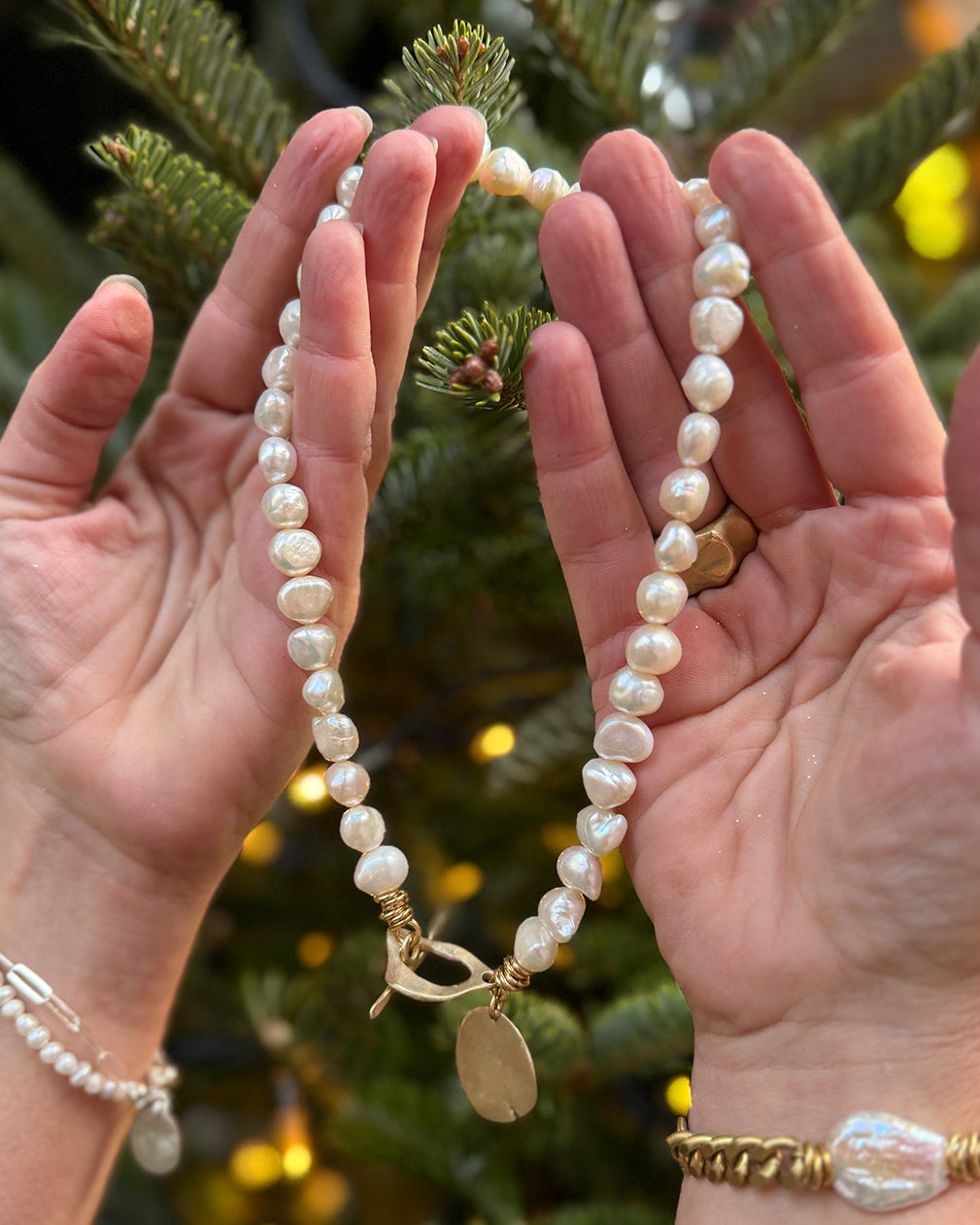 Hands holding a pearl necklace with a Christmas tree in the background