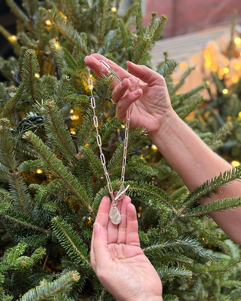 Person holding a necklace with a pearl pendant in front of a decorated Christmas tree.