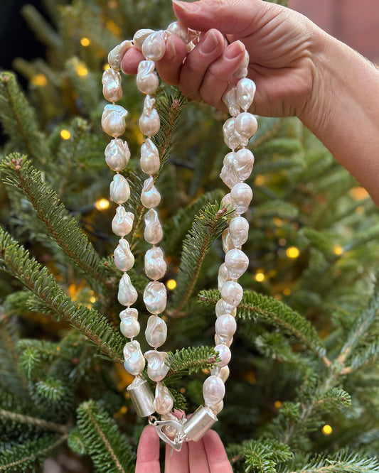 Pearl necklace with a silver clasp held by a hand in front of a decorated Christmas tree.