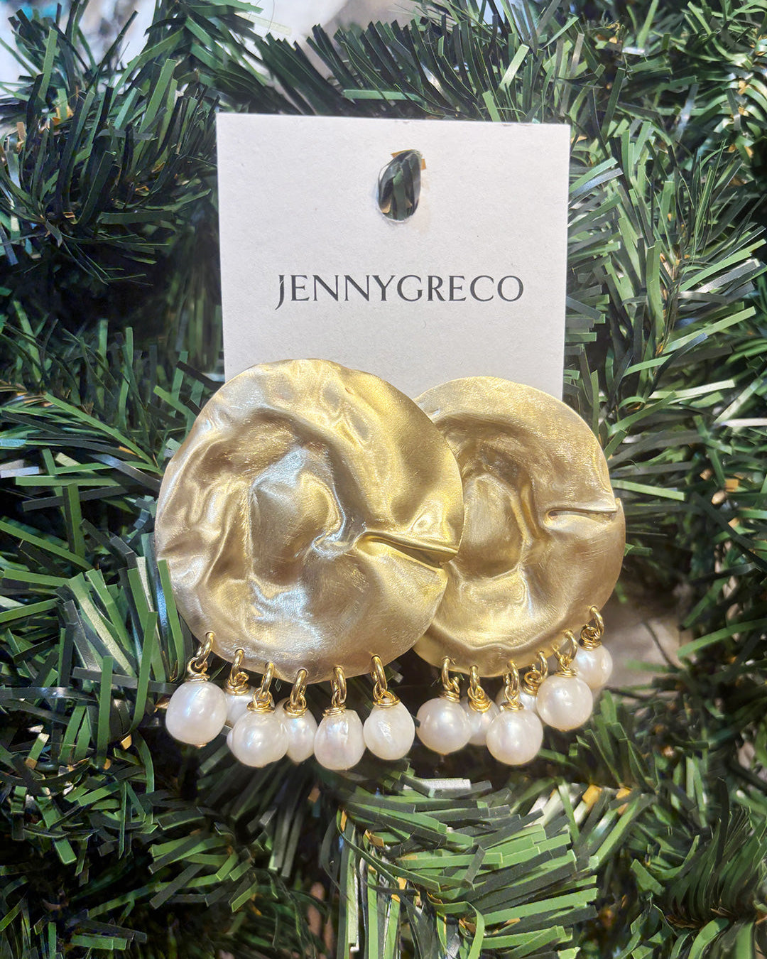 Textured gold disk earrings with pearl drops on a Jenny Greco card against a green foliage background