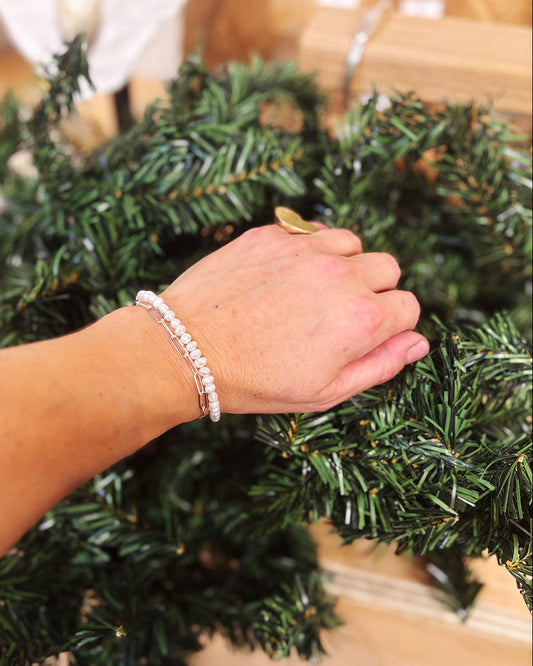 Hand wearing a pearl and silver bracelet against a green artificial Christmas tree with a blurred background