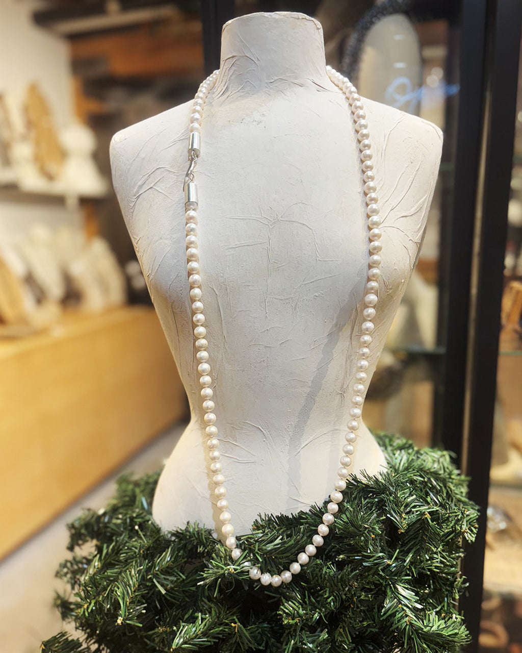 Mannequin wearing a long pearl necklace and green wreath in a store setting
