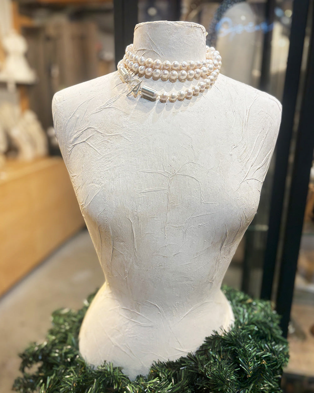 Mannequin head with pearl necklace and greenery in a store setting