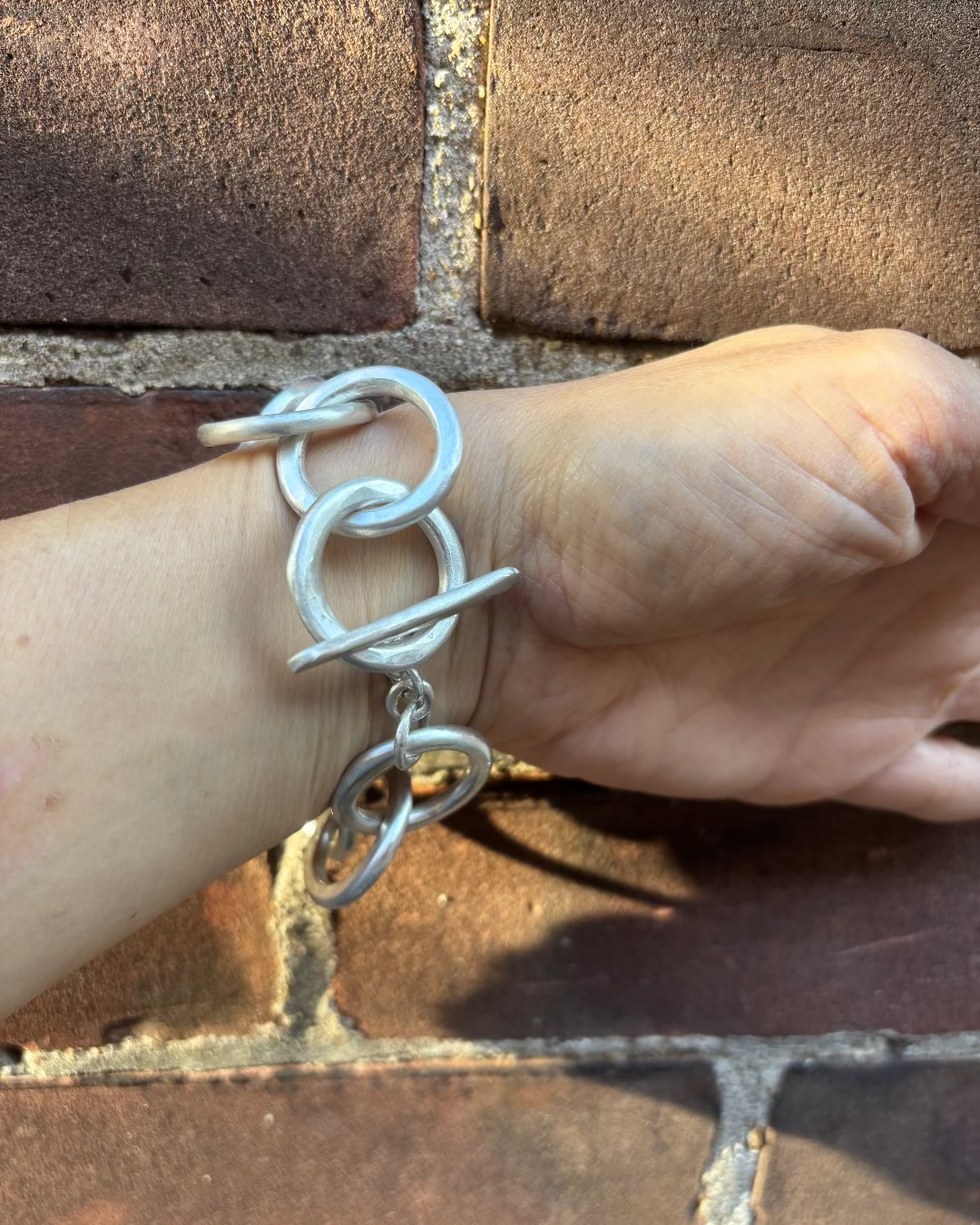 Silver link bracelet on a wrist against a brick wall background