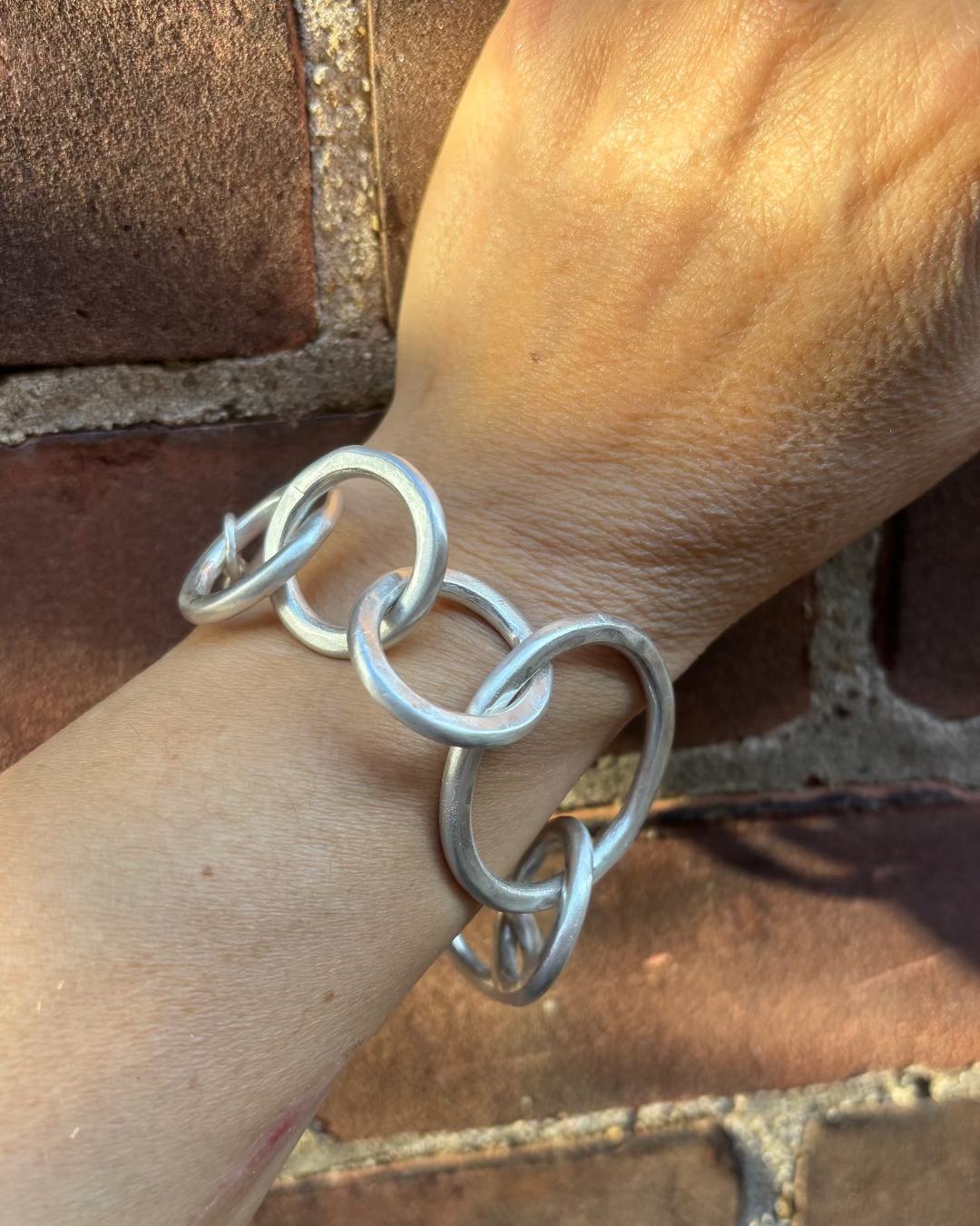Silver link bracelet on a wrist with a brick wall background