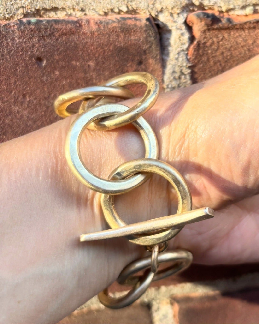 Gold link bracelet on a hand with a brick background