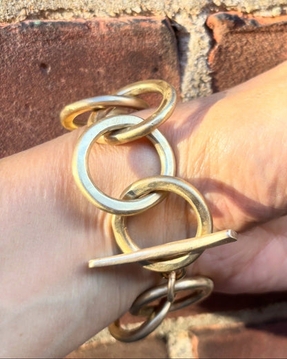Gold link bracelet on a hand with a brick background