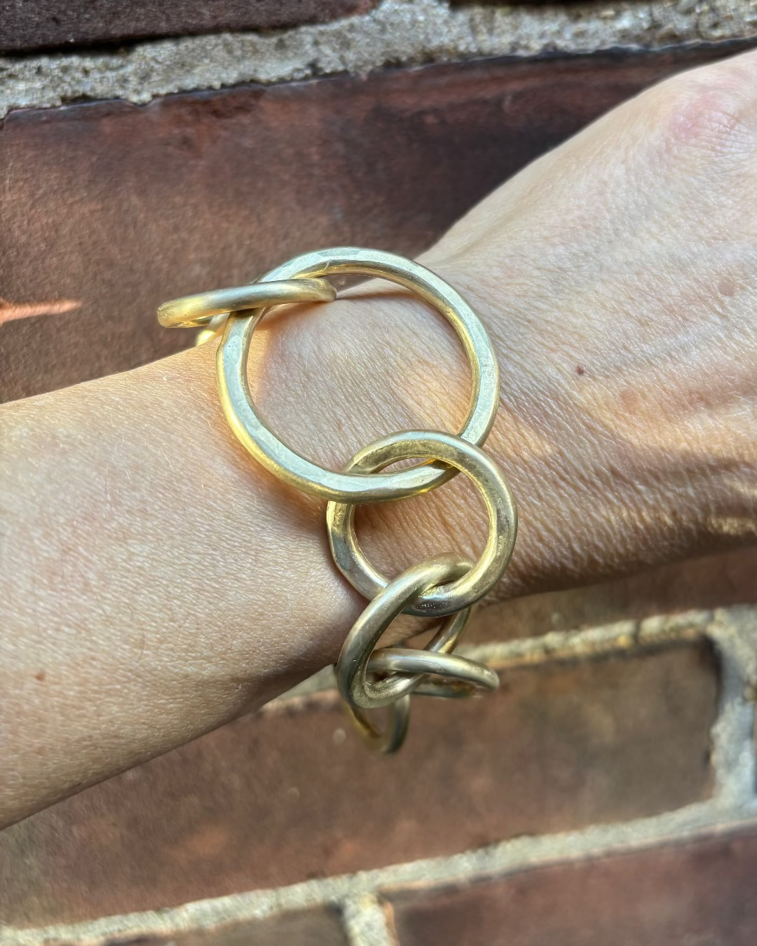 Bronze circular link bracelet on a wrist with a brick background