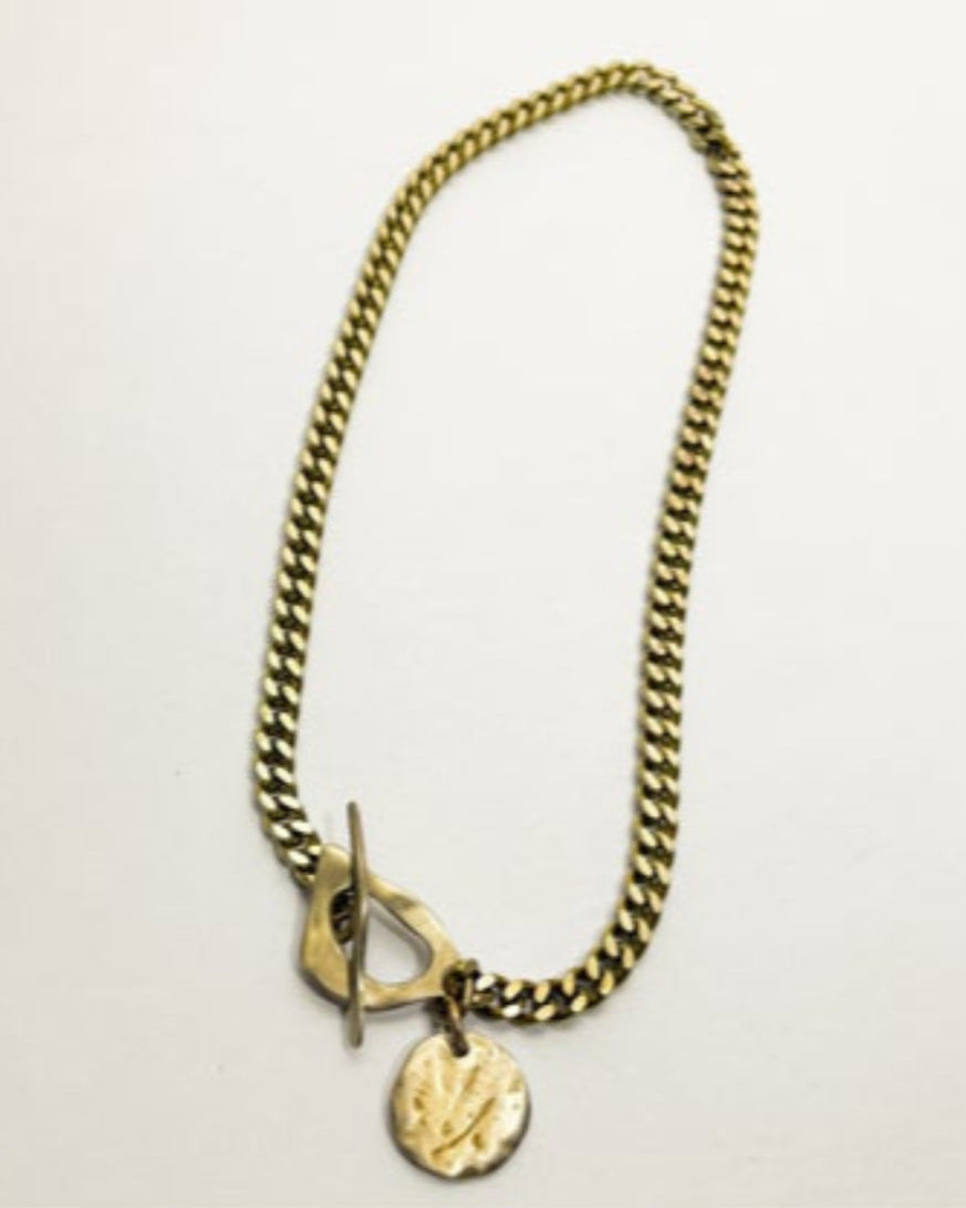 Gold chain necklace with a round pendant on a light gray background